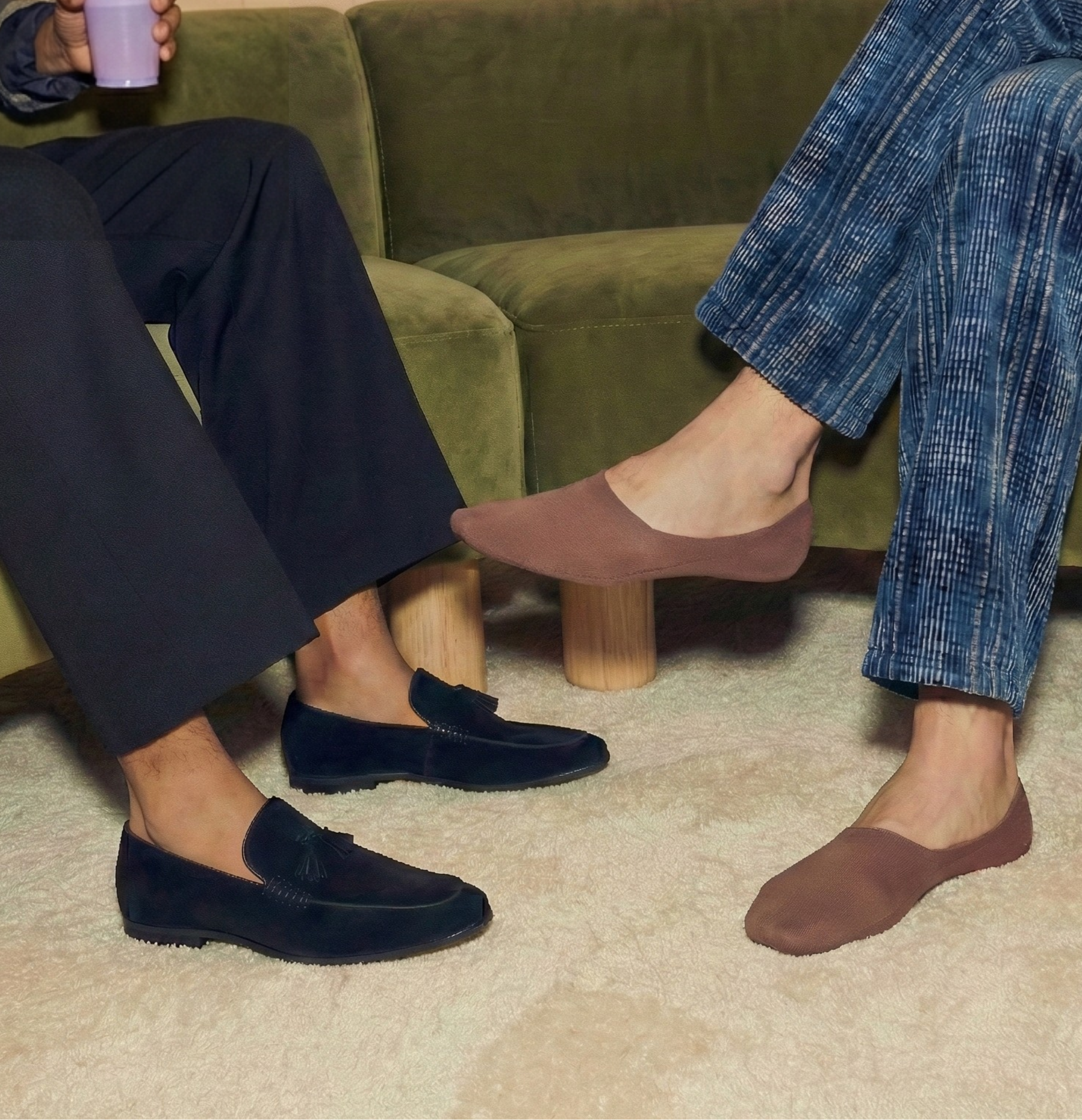 Two people sitting on a green couch wearing shoes, one in navy and the other in brown.